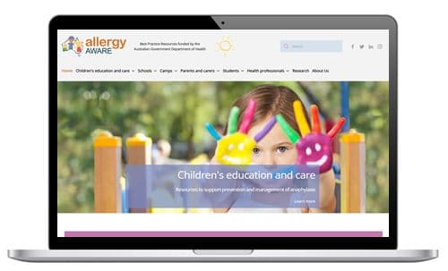 Laptop displaying the allergy aware website with a child holding up colourful painted hands. Text reads "Children's education and care."